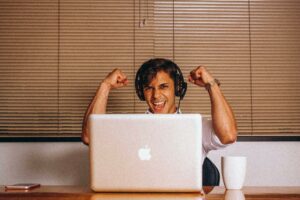 Accueil Young man with headphones shows excitement while using a laptop in office environment.