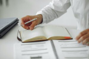 Accueil Close-up of a businessman writing notes in a diary at a modern office desk.